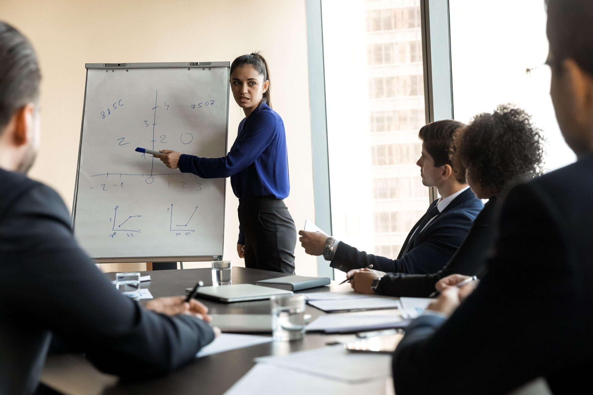 Seriöse junge erfahrene Sprecherin zeigt auf Diagramme auf Whiteboard.